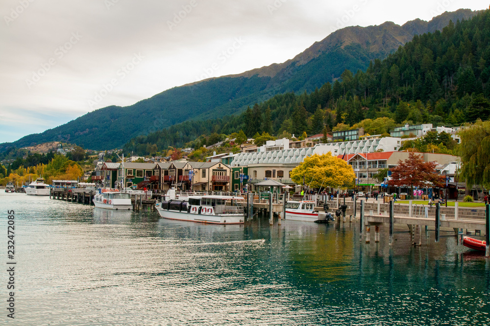 Central part of Queenstown resort town on lake Wakatipu in Southern Alps, docked boats and lakeside city park, alpine architecture, colourful autumn in mountains, New Zealand