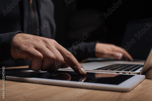cropped shot of male hacker using laptop and tablet, cyber security concept