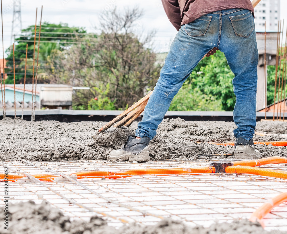 Workers spreading concrete over the slab of a house under construction. Structural parts of a house, building background. Steel beams and electrical mains piping on the house ceiling. Workers spreading concrete over the slab of a house under construction. Structural parts of a house, building background. Steel beams and electrical mains piping on the house ceiling.