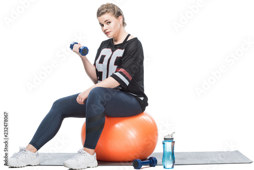 young overweight woman sitting on fit ball and exercising with dumbbell isolated on white photo
