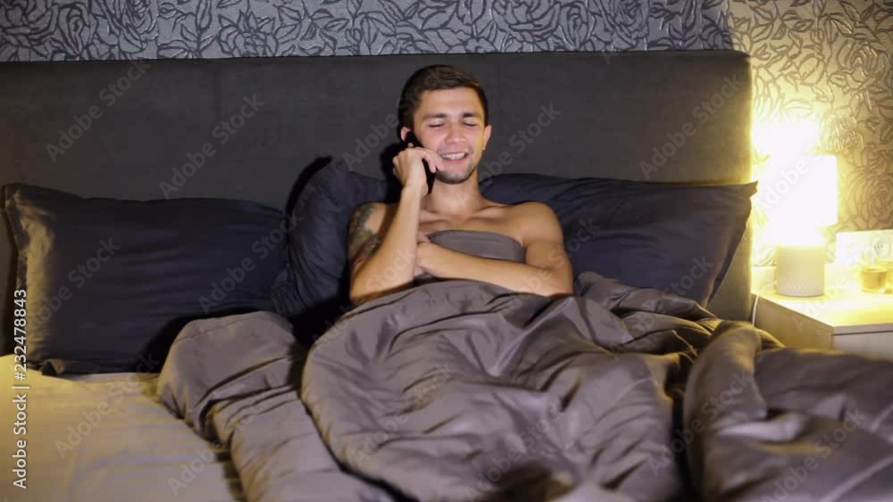 Young man speaking on mobile phone with girlfriend in bed at home in the evening