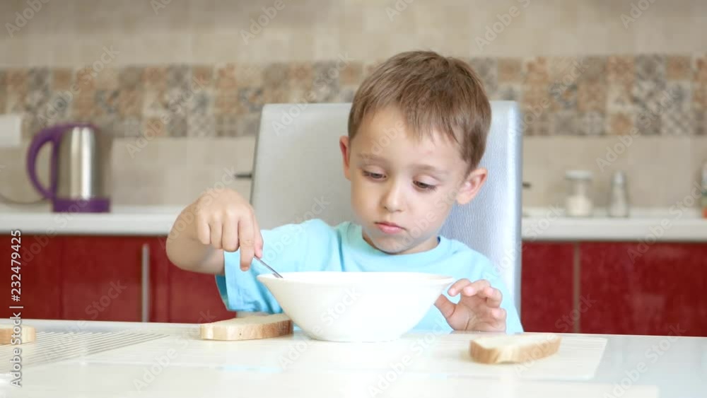 The child is sitting on the kitchen table and eats soup. The child is sitting on the kitchen table and eats soup.
