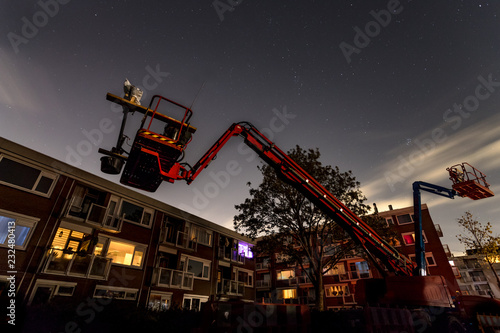 two elevated  hydraulic platforms or cherry pickers at night. In front of apartment buildings and stars in the sky