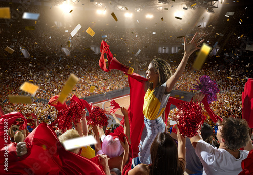 Young sport supporter happy fans at basketball arena. Beautiful black woman with red flag support the basketball team during the game and shouting into a red mouthpiece