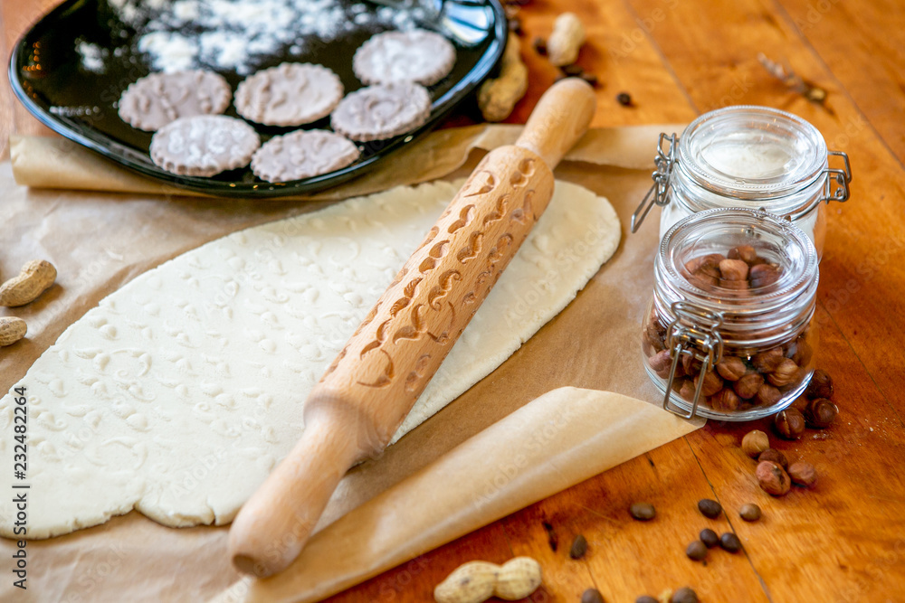 Rolling pin with a mustache pattern on a wooden decorated table covered with baked flour. Rolled dough with a pattern and cookie of various shapes. Biscuit cooking background, close-up