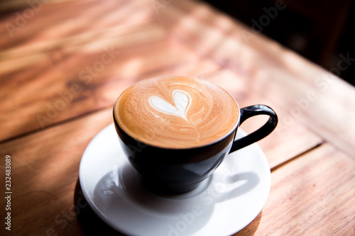 Cappuccino cup with heart latte art on wooden table background.
