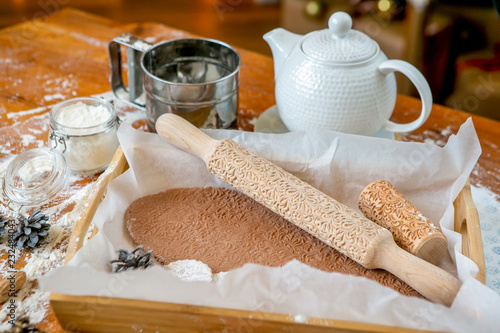 Rolling pin with a pattern on a wooden decorated table covered with baked flour. Rolled dough with a pattern and cookie of various shapes. Biscuit cooking background, close-up