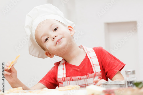 Little cheerful boy chef cooks and eats pizza