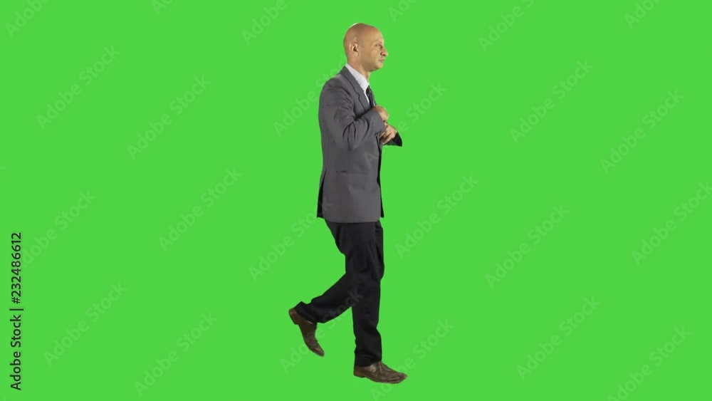 Businessman walking and tied up his suit, waving hello, looking around. Wearing a suit. Full sideways shot over a green screen. Businessman walking and tied up his suit, waving hello, looking around. Wearing a suit. Full sideways shot over a green screen.