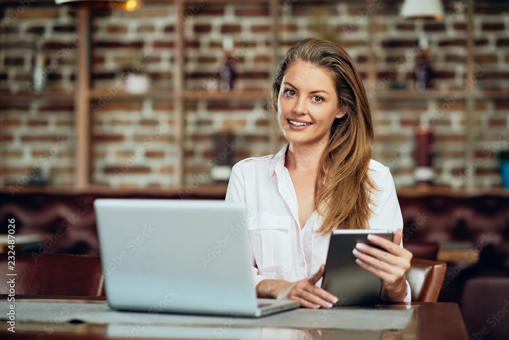 Businesswoman using tablet while sitting in cafeteria. On table laptop. Businesswoman using tablet while sitting in cafeteria. On table laptop.