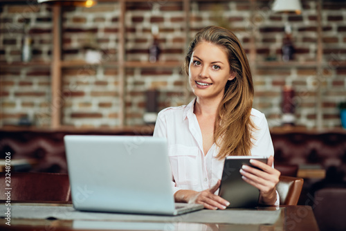 Businesswoman using tablet while sitting in cafeteria. On table laptop.