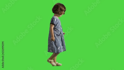 Little girl walking sideways over a green screen, happy and cheerful, spreading hands and laugh, wearing a dress.