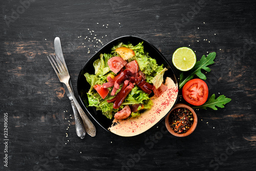 Salad of fresh vegetables and sausages in a black plate. On a wooden background. Top view. Free space for your text.