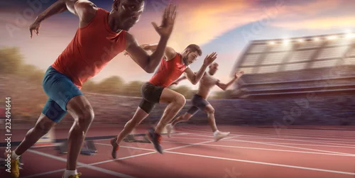 Obraz Sportowcy sprinterscy. Trzech mężczyzn w ubraniach sportowych biegnie po bieżni na profesjonalnym stadionie