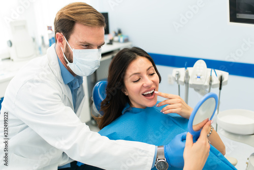 Female patient at the dentist office showing which teeth needs to be repaired. Young beautiful dentist and a woman patient sitting in dental clinic. Teeth whitening.