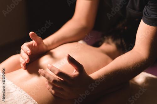 Close-up male hands doing healing massage with oil to a young girl in a dark cosmetology office. Dark key