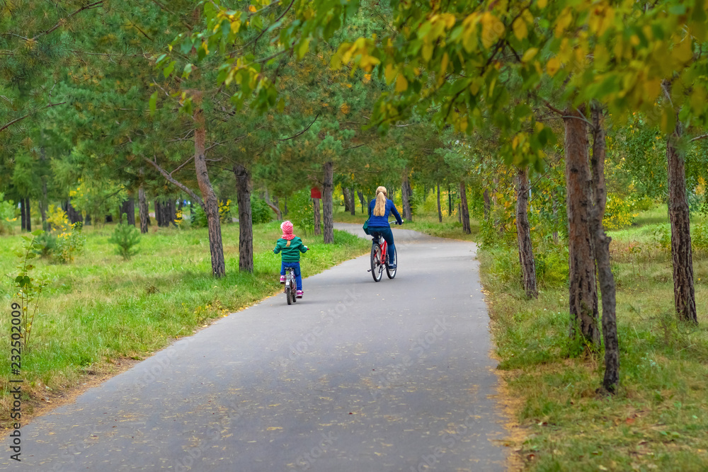 Mom and daughter cycling in the park in autumn Mom and daughter cycling in the park in autumn