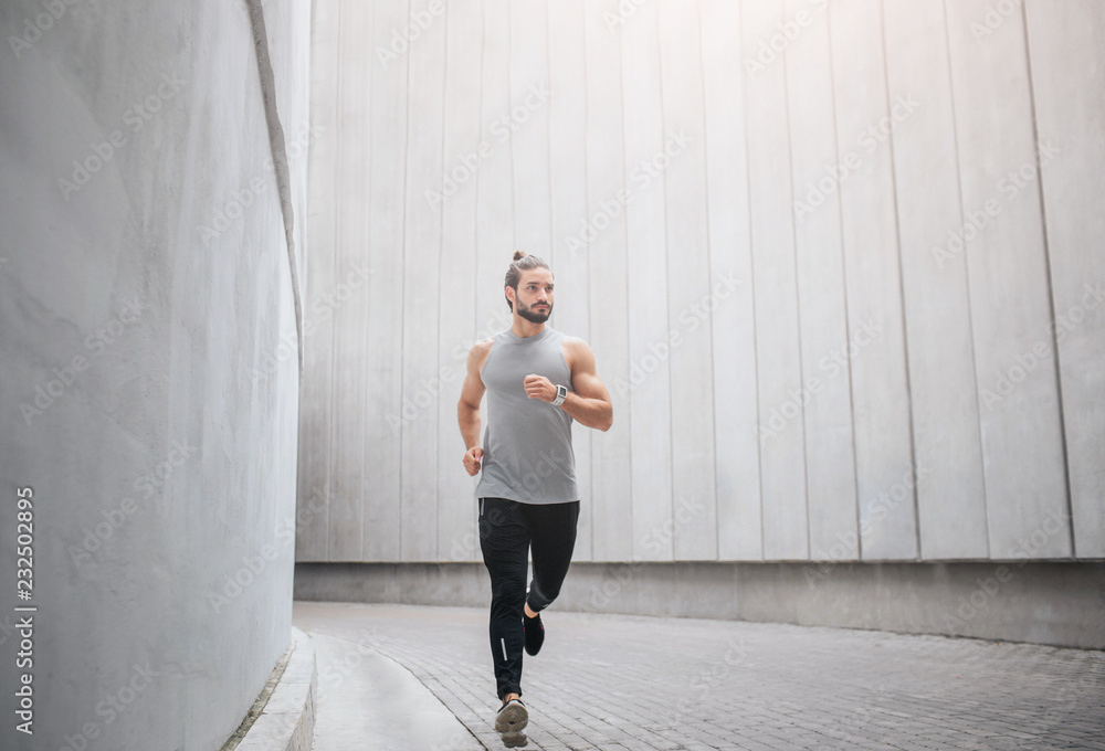 Picture of jogger runs through concrete corridor. He waves with hands and looks to right. Serious young man is concentrated. Picture of jogger runs through concrete corridor. He waves with hands and looks to right. Serious young man is concentrated.