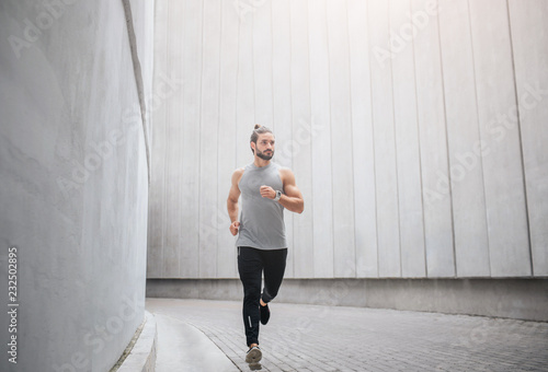 Picture of jogger runs through concrete corridor. He waves with hands and looks to right. Serious young man is concentrated.