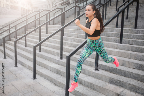 Picture of fast running model. She does it on steps. Young woman helps herself with hands. She runs as fast as she can. Young woman poses on camera in this way.