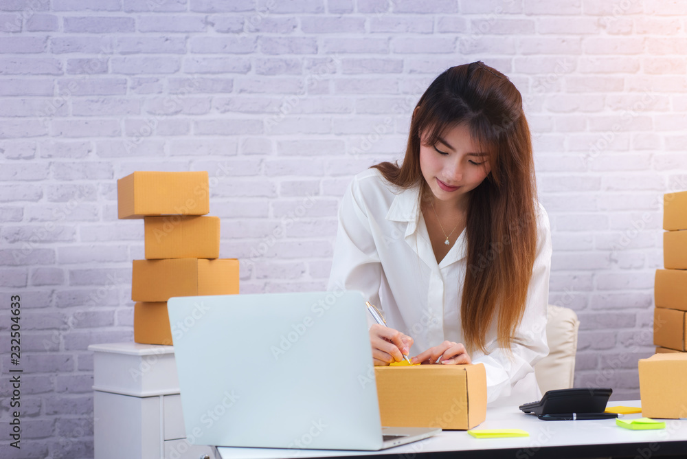 Women business owner writing address on packing box at workplace in home offce. online shopping SME entrepreneur or freelance working concept. Women business owner writing address on packing box at workplace in home offce. online shopping SME entrepreneur or freelance working concept.