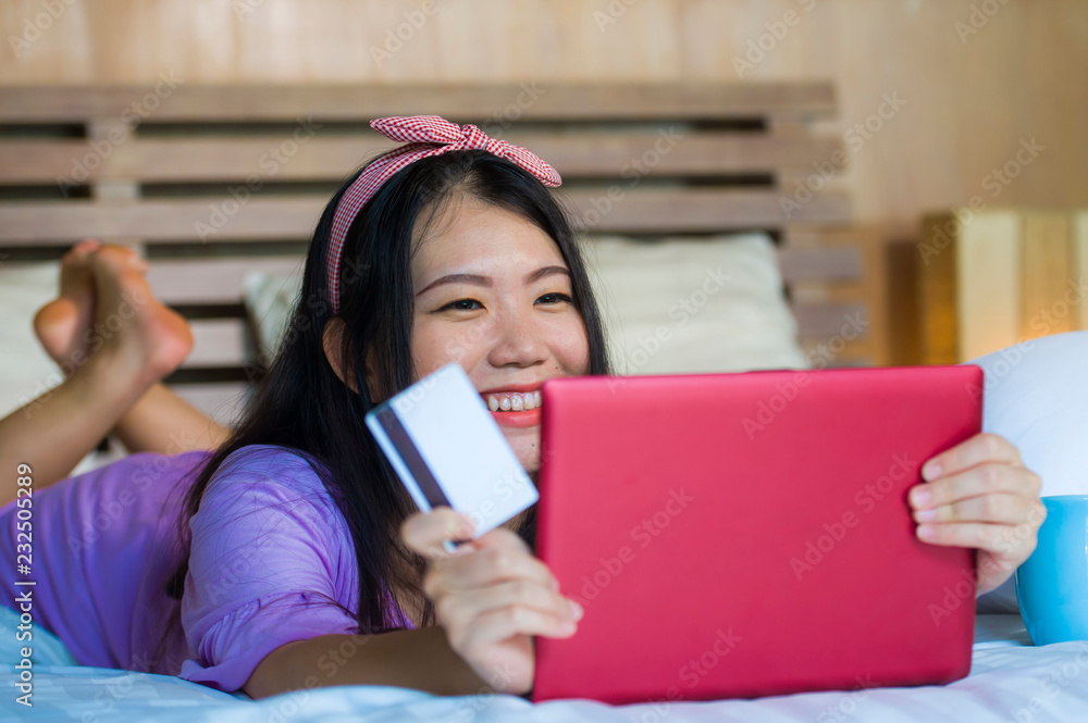 young beautiful happy Asian Korean woman using credit card internet banking on laptop computer at home in bed smiling shopping online e-commerce concept young beautiful happy Asian Korean woman using credit card internet banking on laptop computer at home in bed smiling shopping online e-commerce concept