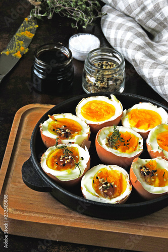Soft-boiled eggs in a skillet. Spices and thyme. Stylish breakfast on a dark surface.