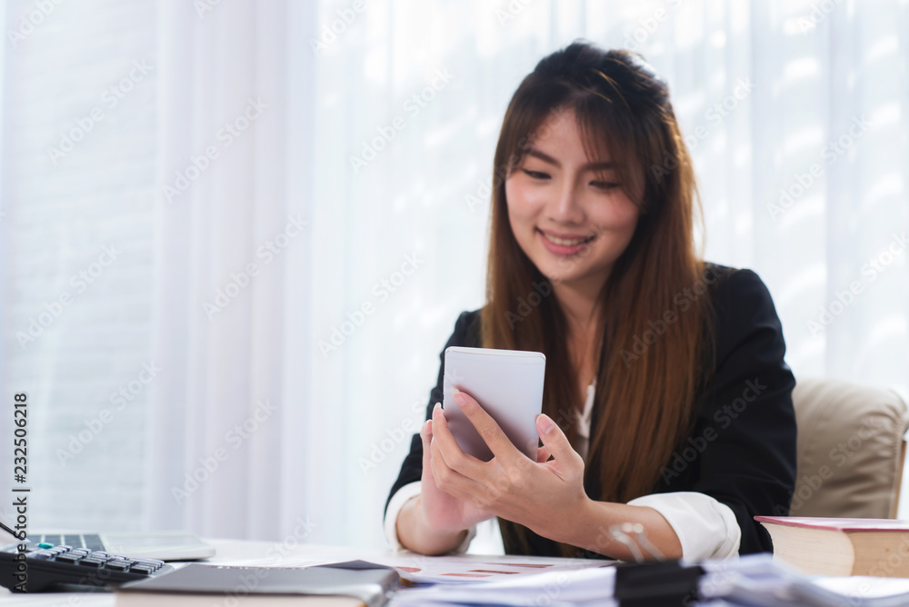 Photo of attractive business woman holding smartphone texting message and sitting at workplace for contact with customer in office. Photo of attractive business woman holding smartphone texting message and sitting at workplace for contact with customer in office.