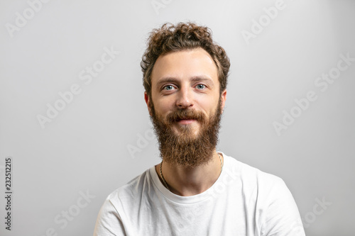 Portrait of young handsome hipster man with beard smiling at camera having positive, kind and confident look, promissing that client have made a right choice, isolated over white background.