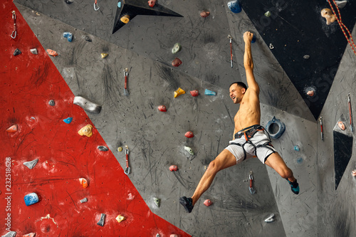 Shortless athletic man bouldering at indoor climbing centre. climber practicing rock climbing at an indoor climbing gym. photo