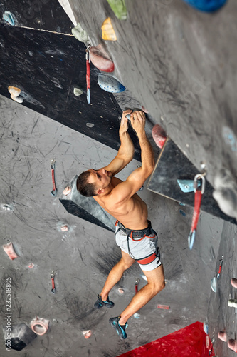 Top view of a professional man climber on a commiting route paricipating in contest, climbs upside down indoors in bouldering gym.