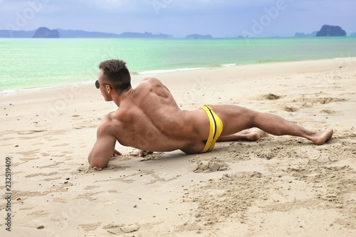 Muscular young sexy naked guy posing on beach in a speedo