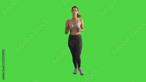 A young woman running in a full body frontal shot over a green screen, looking into the camera and smiles, wearing a sport bra.