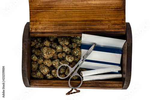 Obraz na płótnie A wooden stash box half filled with green marijuana buds covered in rich red hairs with a pair of scissors, 2 prerolled joints & a pack of rolling papers on a white background. w salonie