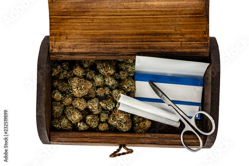 Obraz na płótnie A wooden stash box half filled with green marijuana buds covered in rich red hairs with a pair of scissors, 2 prerolled joints & a pack of rolling papers on a white background. w salonie