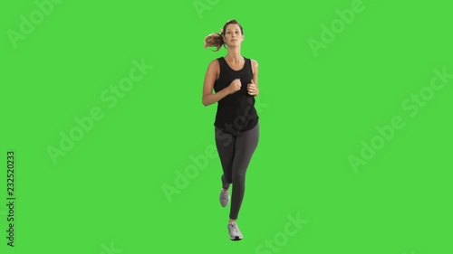 Young woman running over a green screen, looking into the camera, slowing down and smiling.