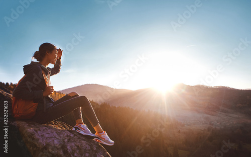 Valokuvatapetti woman hiker with backpack sits on edge of cliff against background of sunrise
