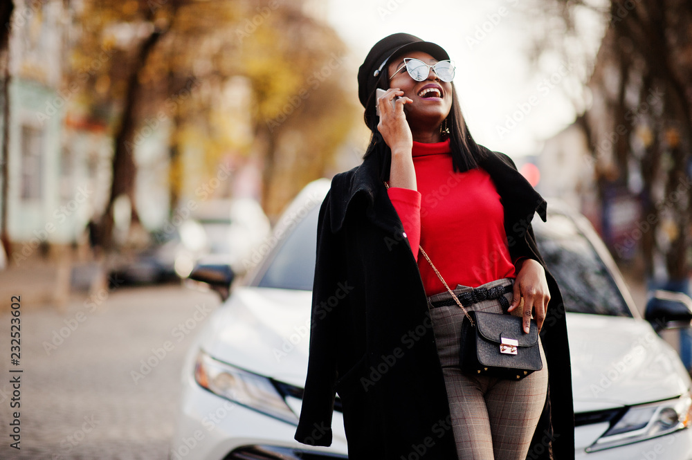 Fototapeta premium African american fashion girl in coat, newsboy cap and sunglasses posed at street against white business car.