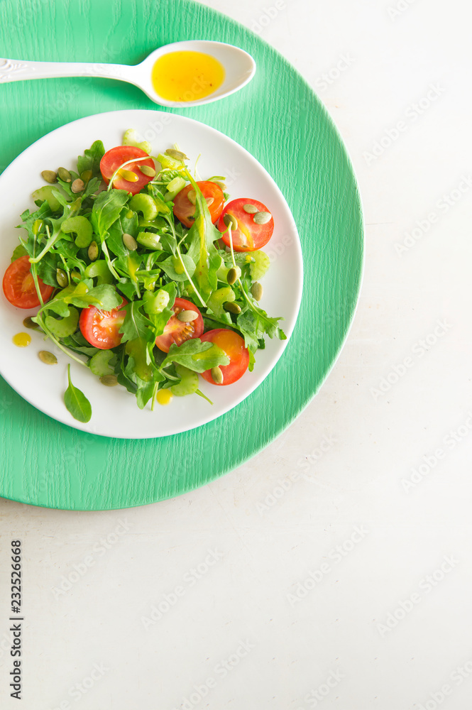 Vegetarian salad with arugula, cherry tomatoes and sunflower seeds on white ceramic plate, top view, copy space Vegetarian salad with arugula, cherry tomatoes and sunflower seeds on white ceramic plate, top view, copy space