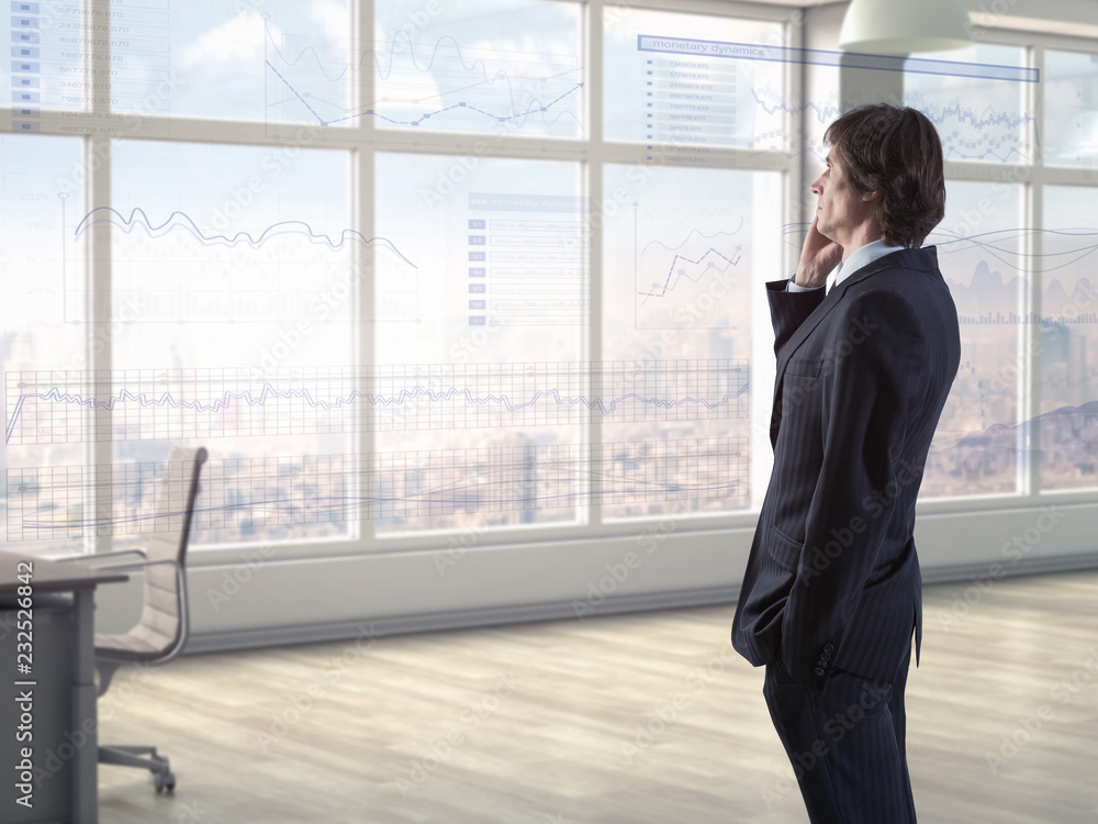Businessman in modern office talking on phone while anaylzing financial charts on virtual display Businessman in modern office talking on phone while anaylzing financial charts on virtual display