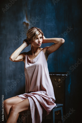 Portrait of sensual blonde woman in a long silk evening dress, fashion beauty photo in a simple interior