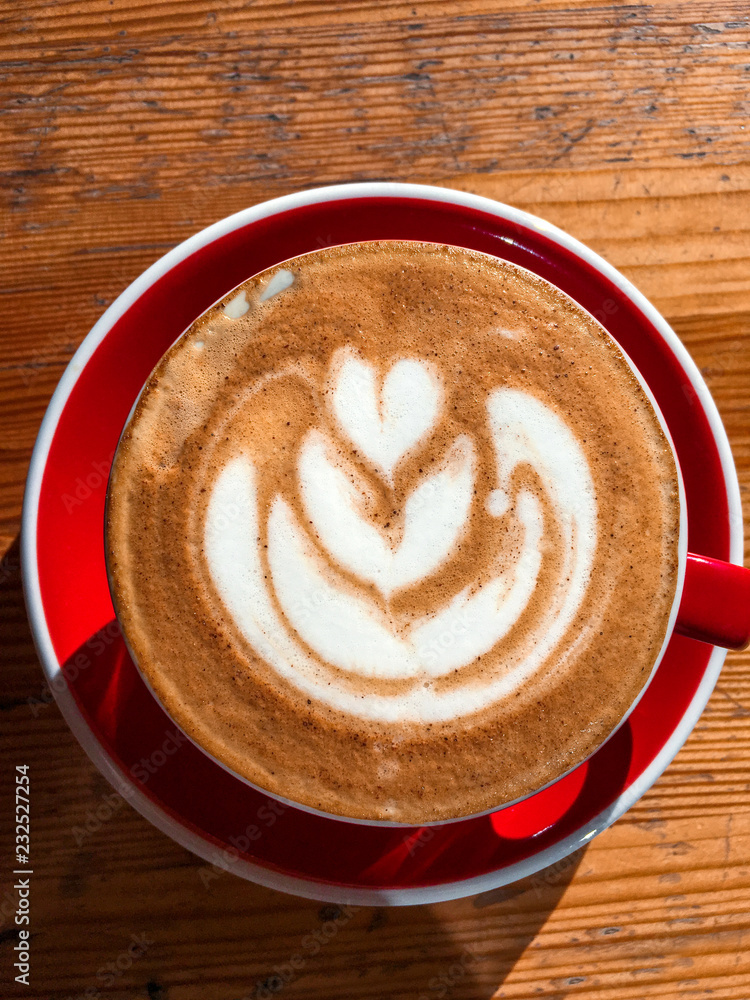 Top view of big red cup with cappuccino hot beverage with foam, with plate on wood textured table. Latte art concept. Close up, copy space, background. Top view of big red cup with cappuccino hot beverage with foam, with plate on wood textured table. Latte art concept. Close up, copy space, background.