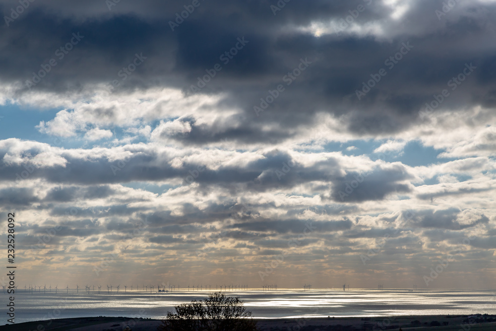 Sunlight shining through clouds onto the sea, with an off shore wind farm on the horizon