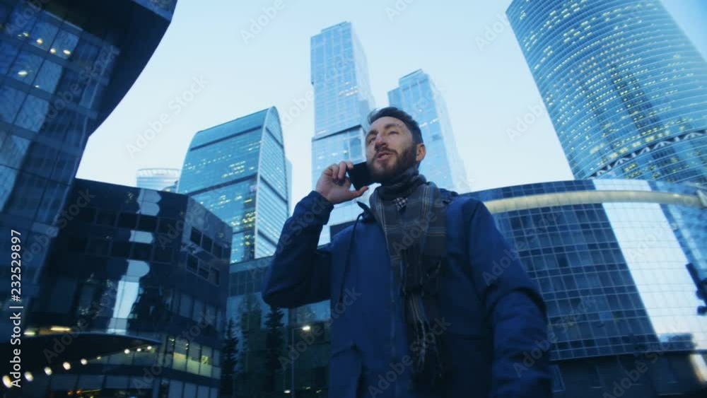 Male tourist is talking on his phone during walking through business complex. Red epic cinema camera footage.