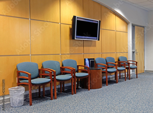 Contemporary medical clinic waiting room: chairs, carpeting, TV, trash can, wood paneling.