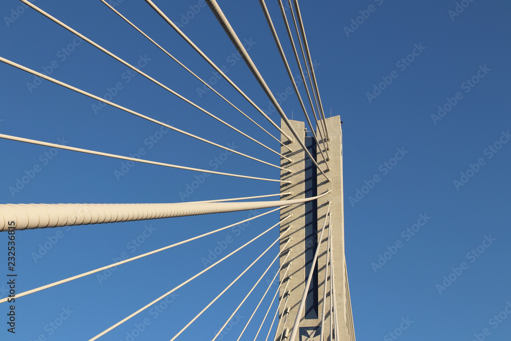 Rzeszow, Poland - 9 9 2018: Suspended road bridge across the Wislok River. Metal construction technological structure. Modern architecture. A white cross on a blue background is a symbol of the city. Rzeszow, Poland - 9 9 2018: Suspended road bridge across the Wislok River. Metal construction technological structure. Modern architecture. A white cross on a blue background is a symbol of the city.