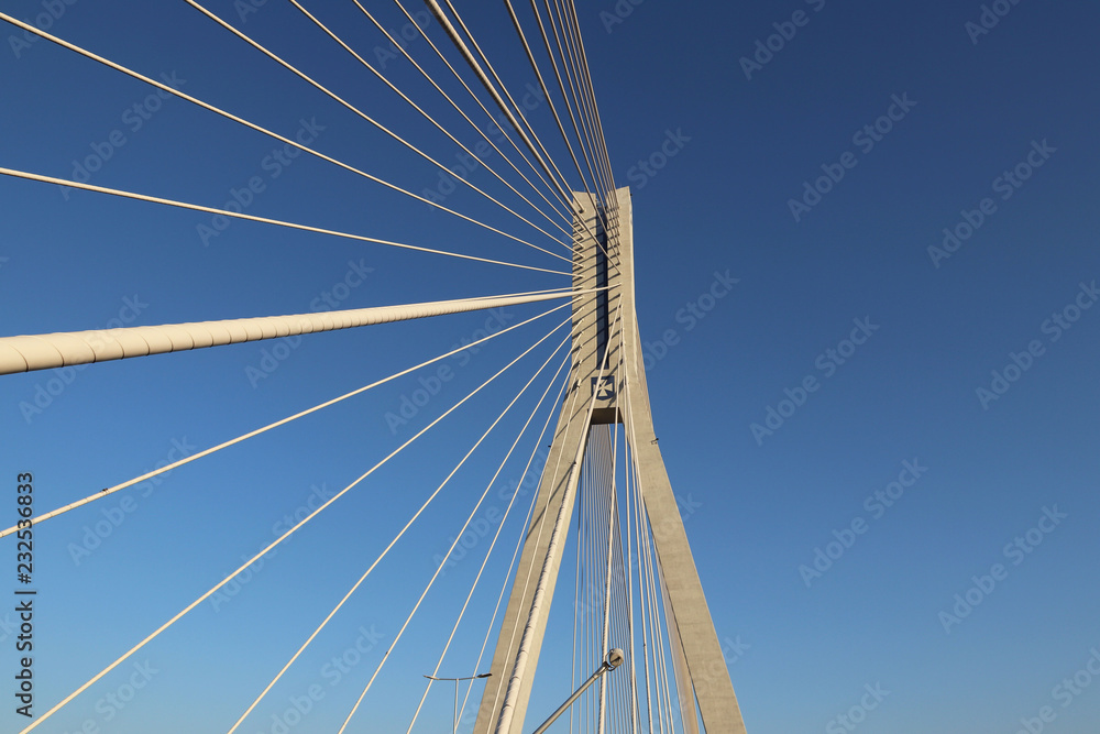 Rzeszow, Poland - 9 9 2018: Suspended road bridge across the Wislok River. Metal construction technological structure. Modern architecture. A white cross on a blue background is a symbol of the city. Rzeszow, Poland - 9 9 2018: Suspended road bridge across the Wislok River. Metal construction technological structure. Modern architecture. A white cross on a blue background is a symbol of the city.