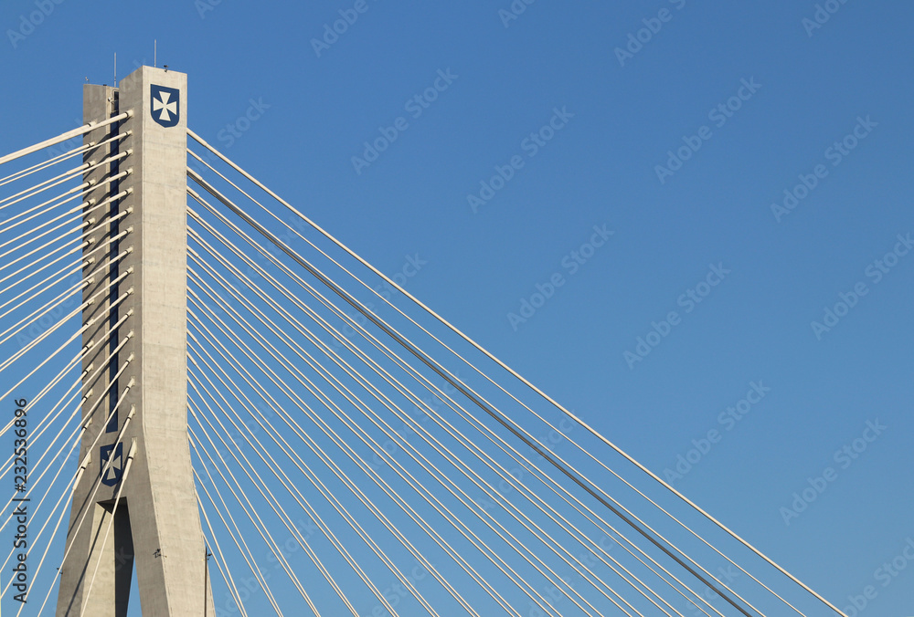 Rzeszow, Poland - 9 9 2018: Suspended road bridge across the Wislok River. Metal construction technological structure. Modern architecture. A white cross on a blue background is a symbol of the city. Rzeszow, Poland - 9 9 2018: Suspended road bridge across the Wislok River. Metal construction technological structure. Modern architecture. A white cross on a blue background is a symbol of the city.