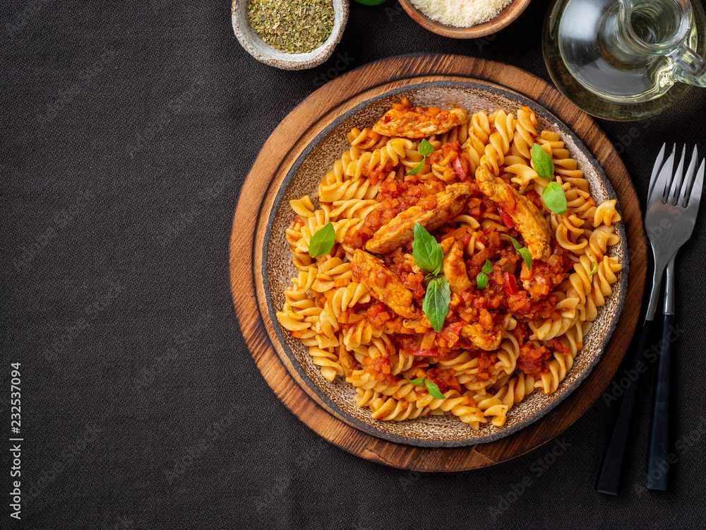 fusilli pasta with tomato sauce, chicken fillet with basil leaves on dark brown background, top view, copy space