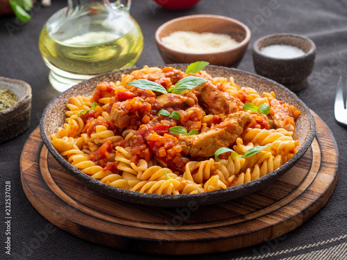 fusilli pasta with tomato sauce, chicken fillet with basil leaves on dark brown background, side view